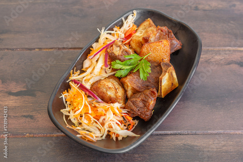 Griot de porc haïtien servi avec pikliz aux poivrons, plat traditionnel créole sur une table en bois. 