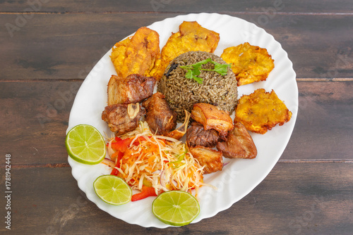 Griot de porc haïtien servi avec bananes pesées, pikliz aux poivrons et riz Djon Djon sur une table en bois. Cuisine créole. 