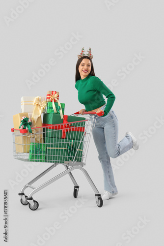 Happy young woman in reindeer horns and cart with gift boxes on white backgro...