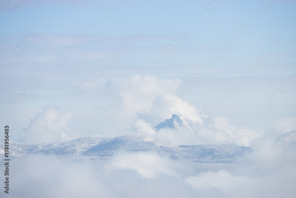 Fototapeta premium Snowy mountain peak surrounded by white fluffy clouds