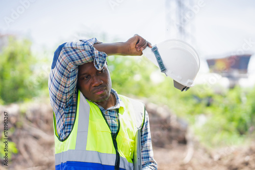 Tired Construction Worker Wiping Sweat on Hot Day,African American Engineer Taking Break from Hard Work at Site,Portrait of a Focused Laborer or Foreman in Safety Gear
