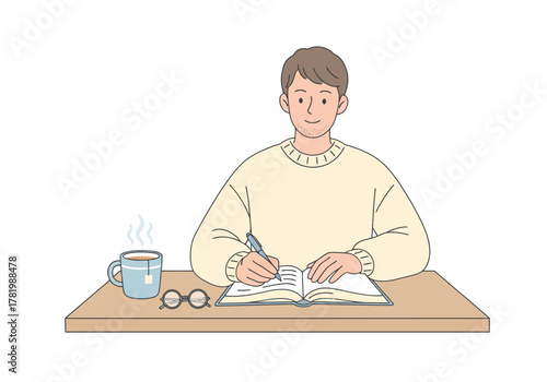 A young man wearing a sweater sits at a desk writing in a notebook, with a cup of hot tea and glasses nearby.