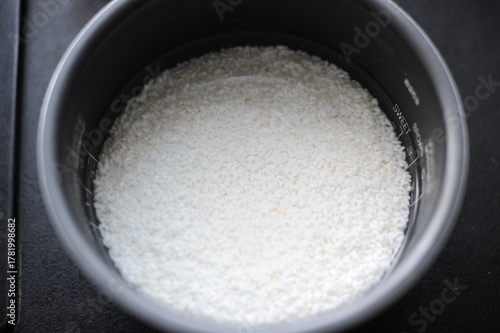 White rice in a rice cooker covered in water ready for boiling as food ingredient