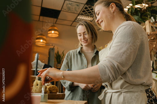 Smiling saleswoman cutting bar of soap by customer in store