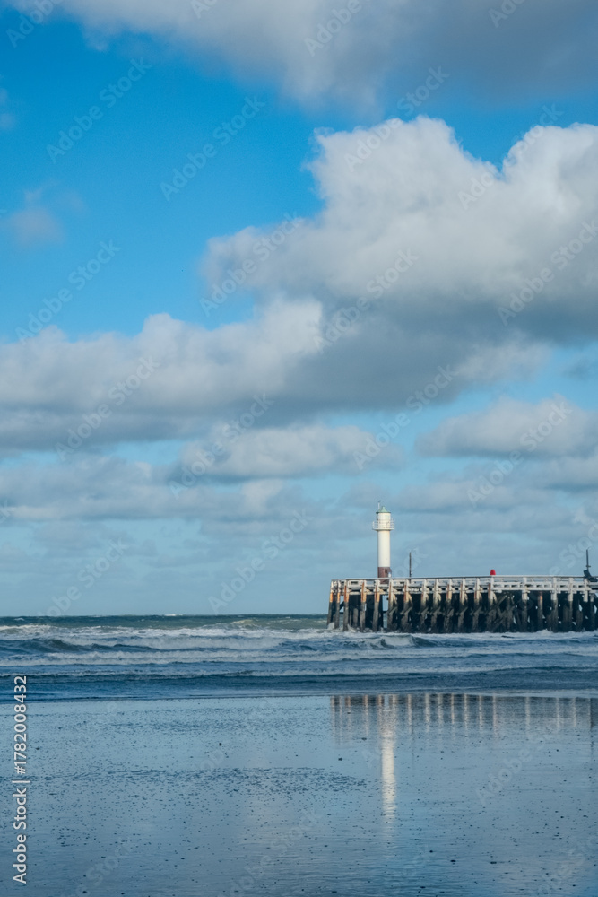 Fototapeta premium Nieuwpoort, West-Vlaanderen, Belgium, Ocotber 25th, 2025, serene coastal scene, quiet seaside pathway leading to lighthouse amidst clouds and reflections