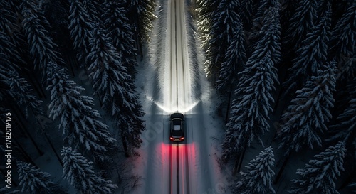 Aerial perspective of a car driving on a snow covered road at night through a winter forest scene.