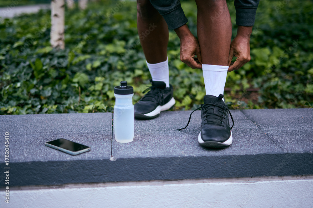 Fototapeta premium Athlete Tying Sneakers On Pavement With Water Bottle And Smartphone Nearby During Workout