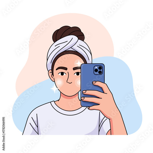 A young woman with a towel on her head taking a selfie with her smartphone, showing off her glowing skin.