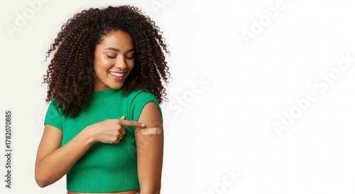 Young black woman smiling and pointing at vaccination bandage on arm  