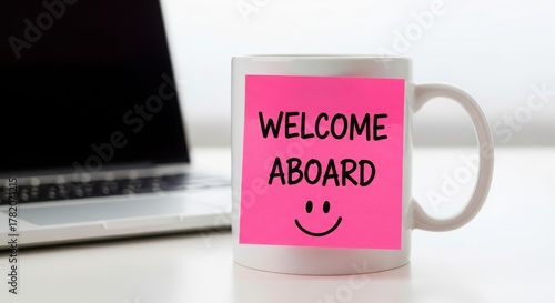 Coffee mug with welcome aboard note next to laptop on desk  