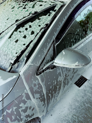Shimmering car covered in foam during a sunny afternoon wash in the driveway of a suburban home