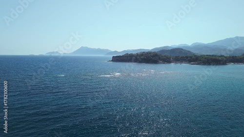 Drone view of the deep blue Mediterranean Sea with forested coastline and distant mountains near Phaselis, Antalya, Turkey. Clear summer sky and sparkling water.