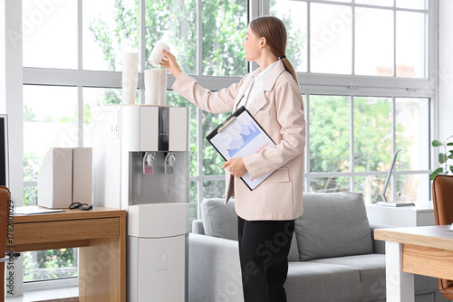 Businesswoman taking paper cup from water cooler in office