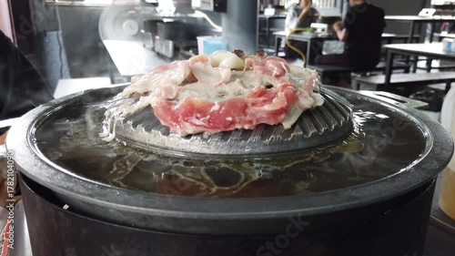 Close-up of Thai-style barbecue grill pan, known as Moo Kratha, with pork belly, shrimp, and vegetables cooking on a hot grill and soup. Popular Asian dining experience in Thailand.