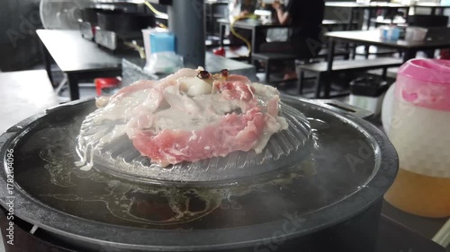 Close-up of Thai-style barbecue grill pan, known as Moo Kratha, with pork belly, shrimp, and vegetables cooking on a hot grill and soup. Popular Asian dining experience in Thailand.