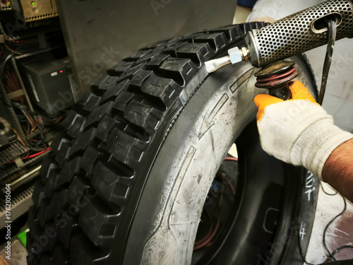 In the rubber retreading factory, the side surfaces of the tire are smoothed with a rubber hand extruder.