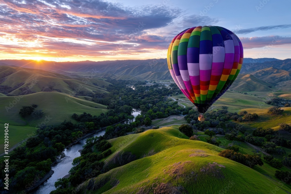 Fototapeta premium Colorful hot air balloon floats above green hills at sunset