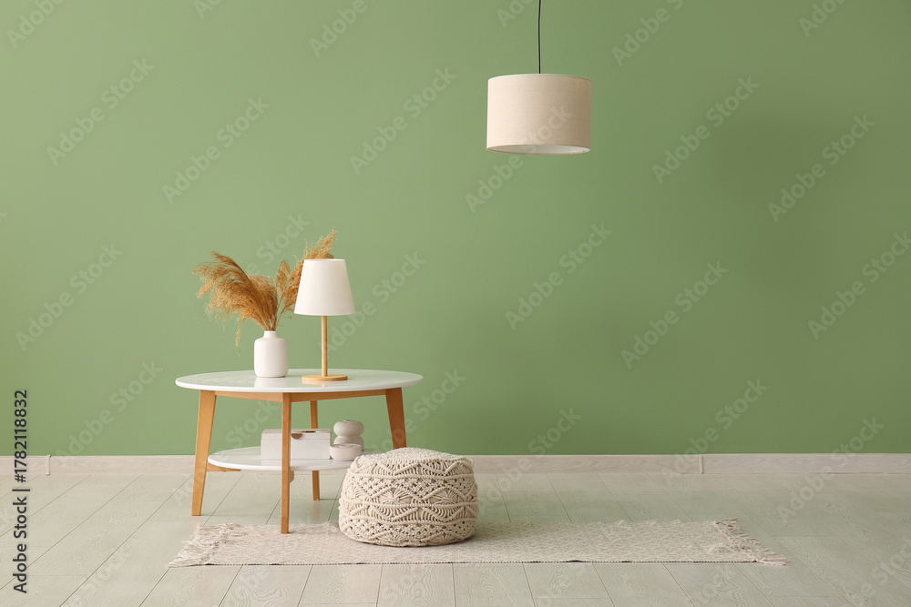 Naklejka premium Table with soft pouf and stylish lamps near green wall in modern room
