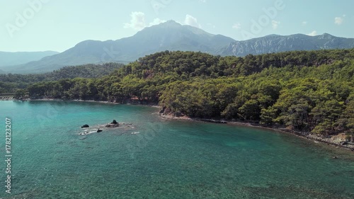 Drone view of Phaselis Bay with turquoise water, pine forest, and Mount Olympos in the background. Beautiful Mediterranean landscape near Kemer, Antalya, Turkey.