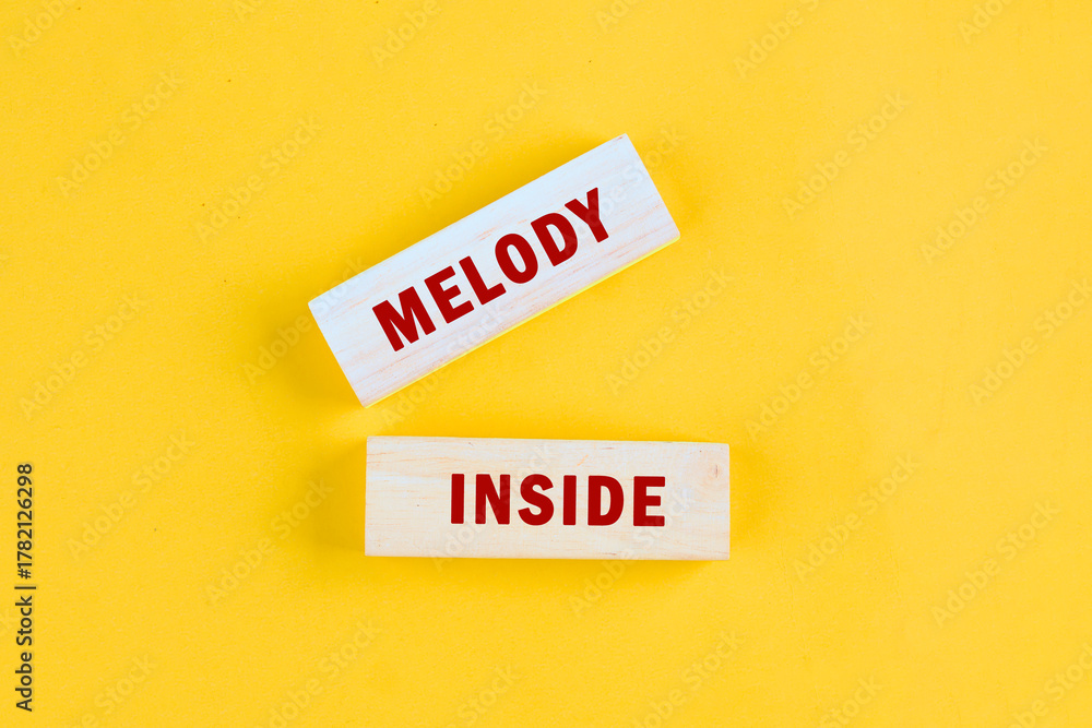 Obraz premium Bright yellow background enhances the wooden blocks that spell out the words melody inside, inspiring feelings of joy and creativity through music and art, perfect for uplifting spirits