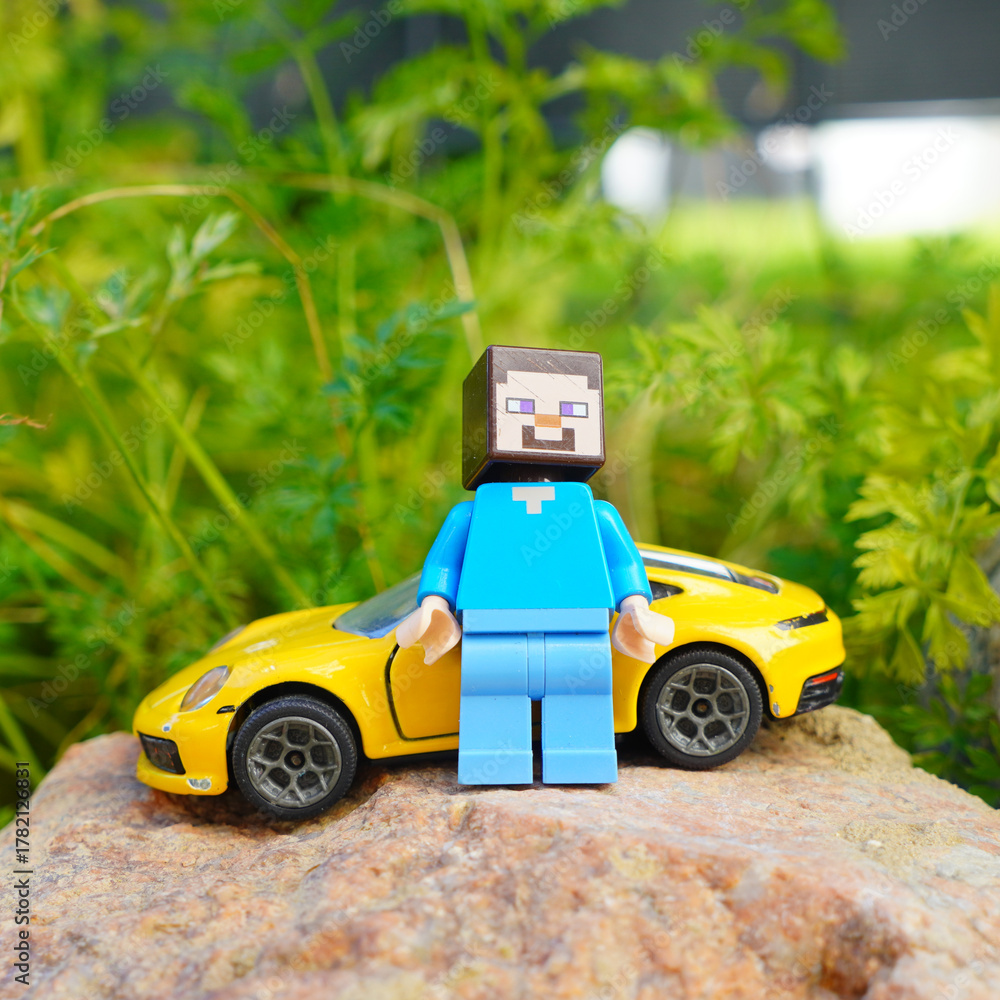 Obraz premium Minecraft Steve figure stands next to a yellow toy sports car on a rock