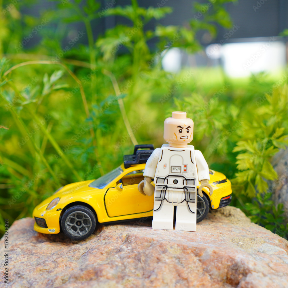 Naklejka premium Lego Star Wars figure with a yellow sports car on a rock in front of green foliage
