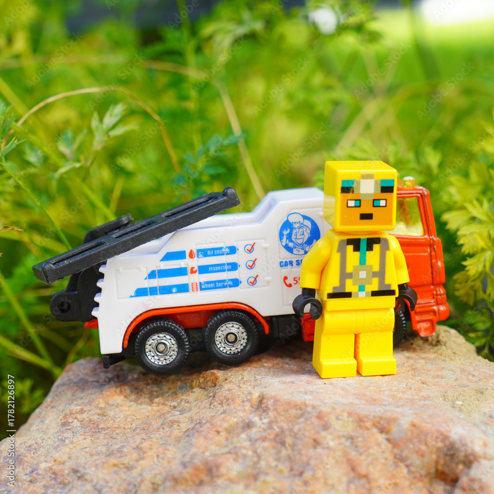 Obraz premium Toy tow truck with a yellow block figure on a rock with green foliage