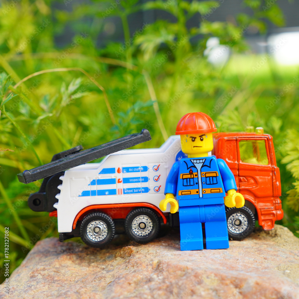 Obraz premium Lego mechanic figure stands next to a tow truck on a rock outdoors