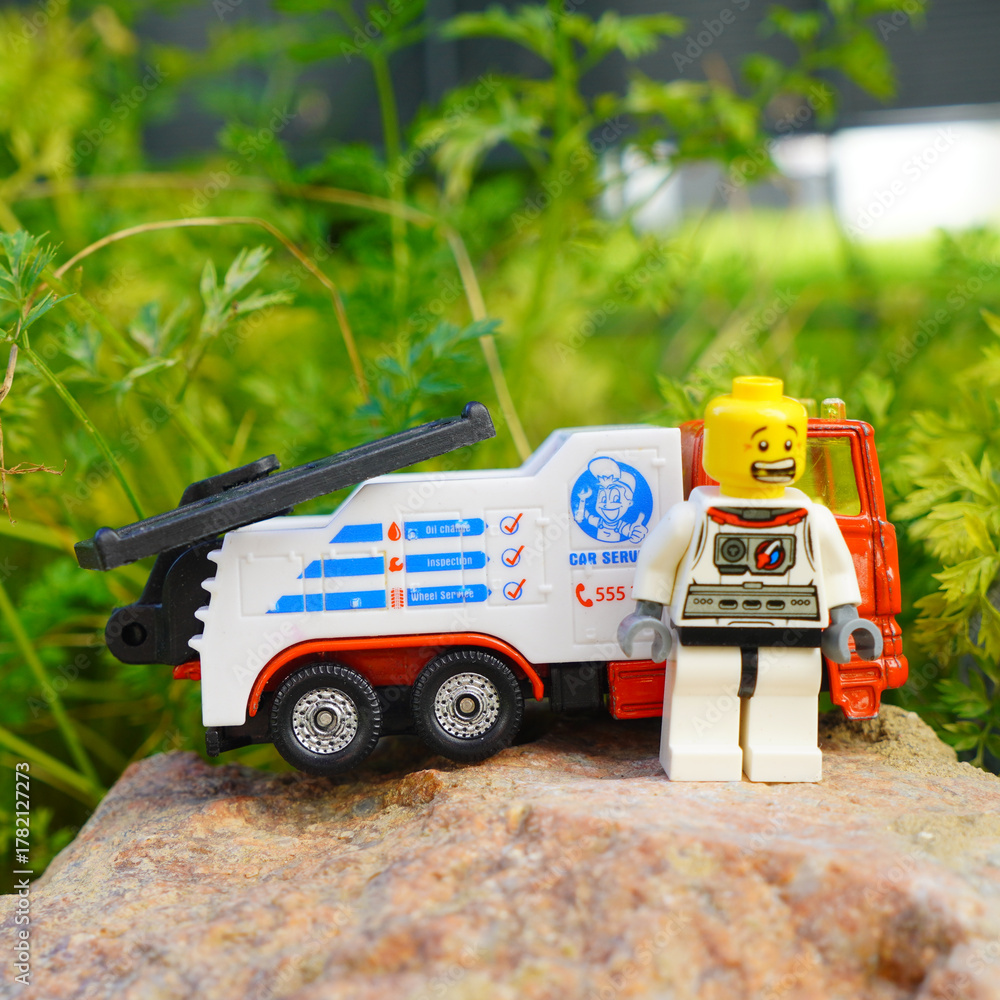 Obraz premium Astronaut figure stands next to a toy tow truck on a rock outdoors