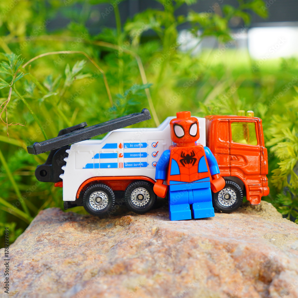 Obraz premium Spider-Man toy figure stands beside a tow truck on a rock outdoors