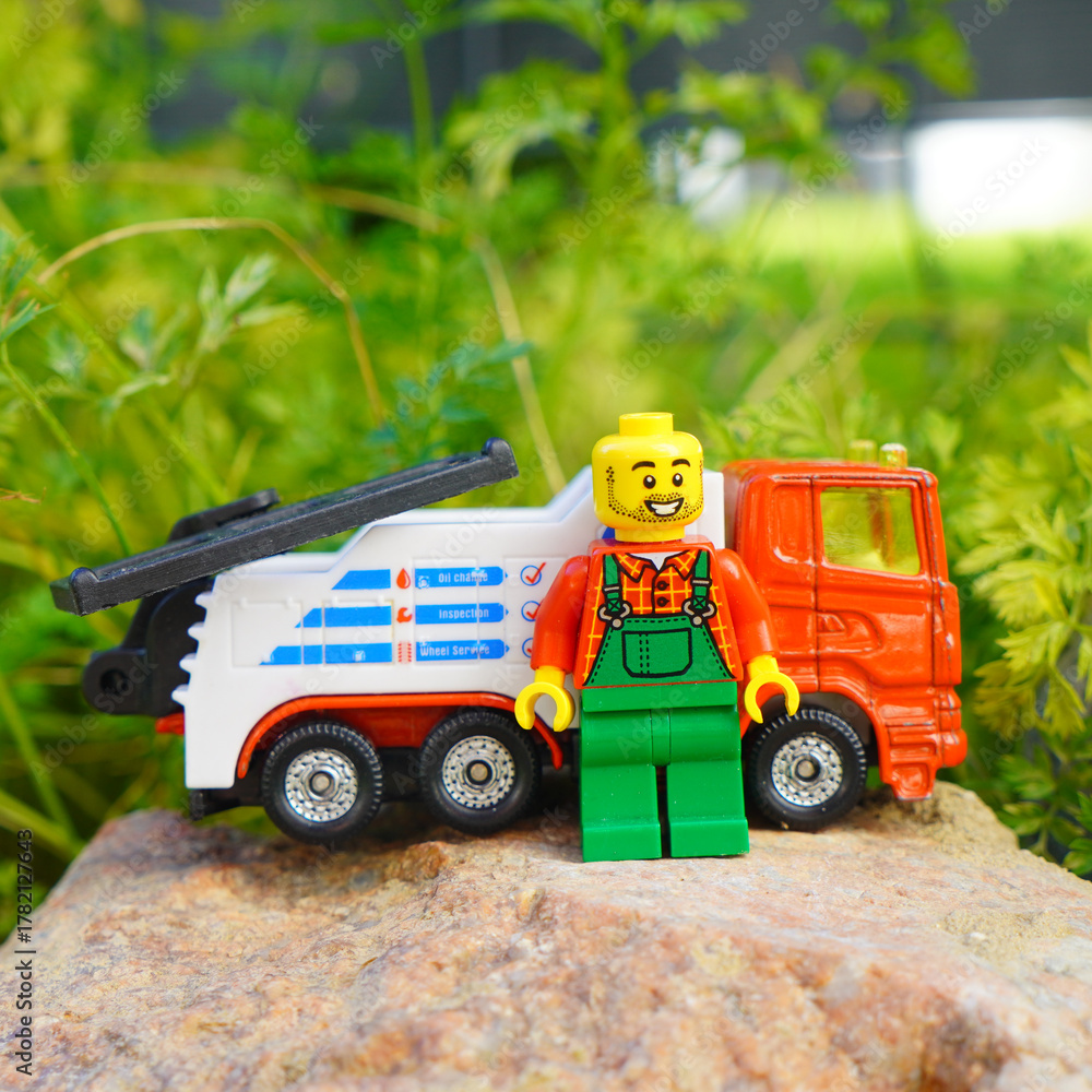 Obraz premium Lego figure with a tow truck toy on a rock with green foliage background