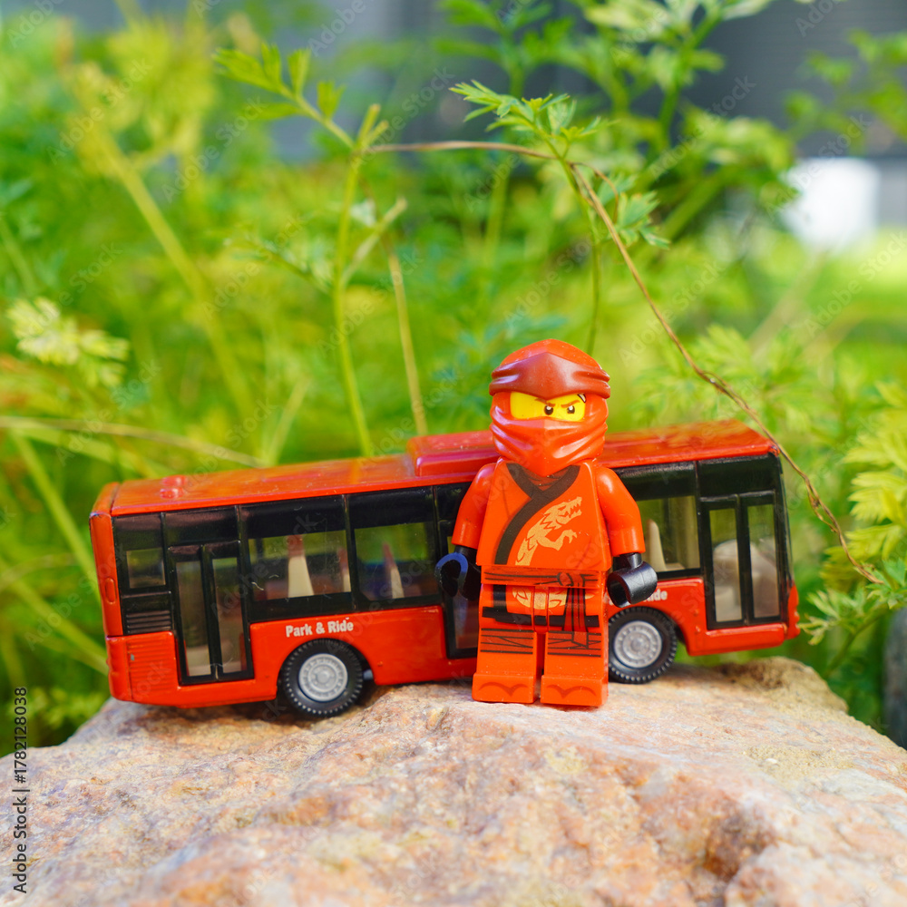 Obraz premium Lego Ninjago character stands next to a red toy bus on a rock