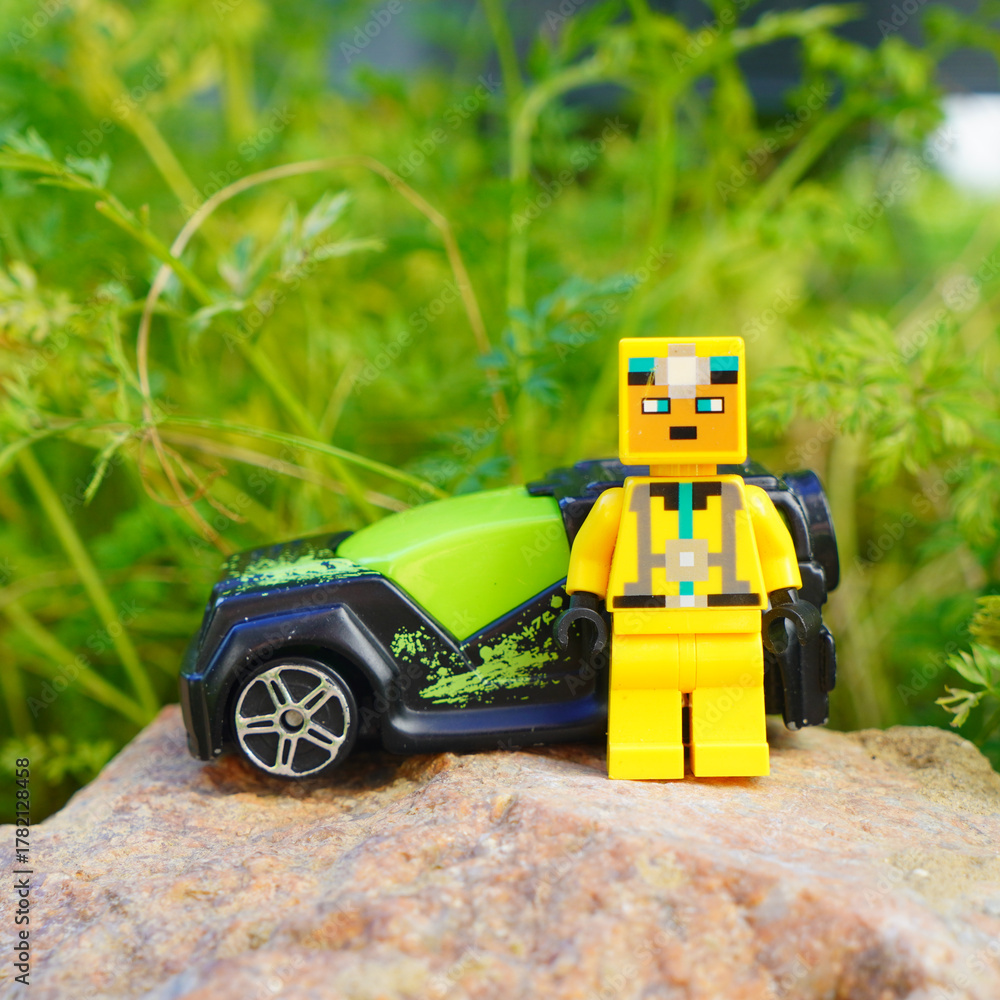 Naklejka premium Lego figure stands next to a toy car on a rock with a green background