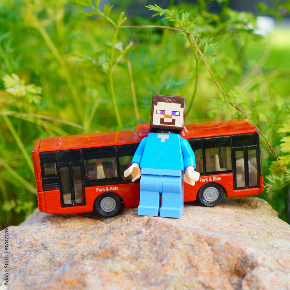 Naklejka premium Minecraft Steve figure with a red toy bus on a rock outdoors