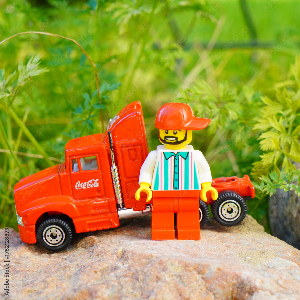 Naklejka premium Lego figure stands next to a toy Coca-Cola semi-truck on a rock