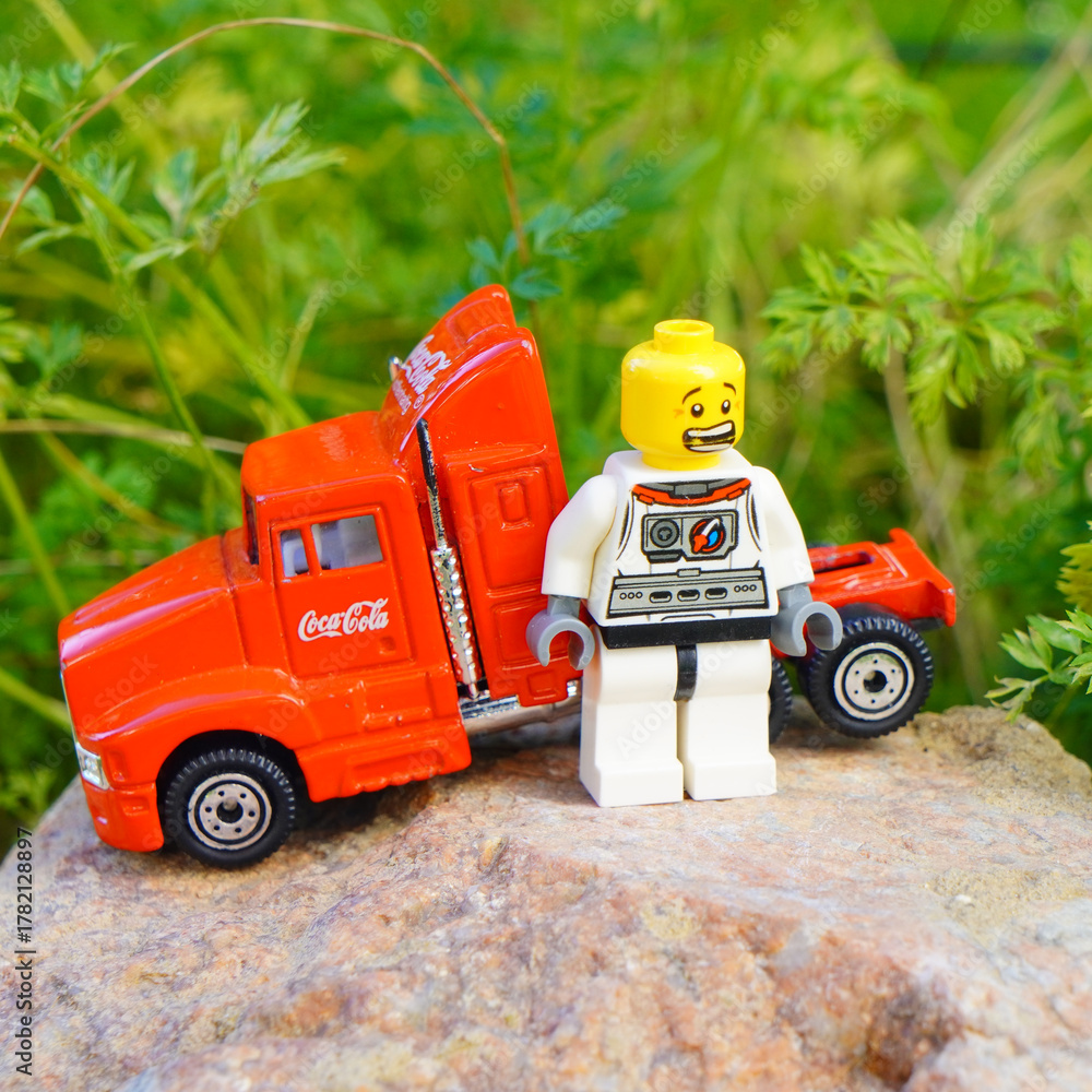 Naklejka premium Lego astronaut figure stands next to a toy Coca-Cola semi-truck on a rock