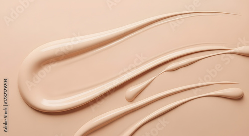 Close-up of creamy beige liquid foundation swatches on a matching background, showcasing texture and consistency for cosmetic use.