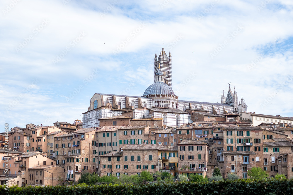 Fototapeta premium Majestic Siena cathedral in Tuscany rises above ancient buildings in a charming Italian town, showcasing stunning architecture and inviting travellers to explore its rich history and vibrant culture