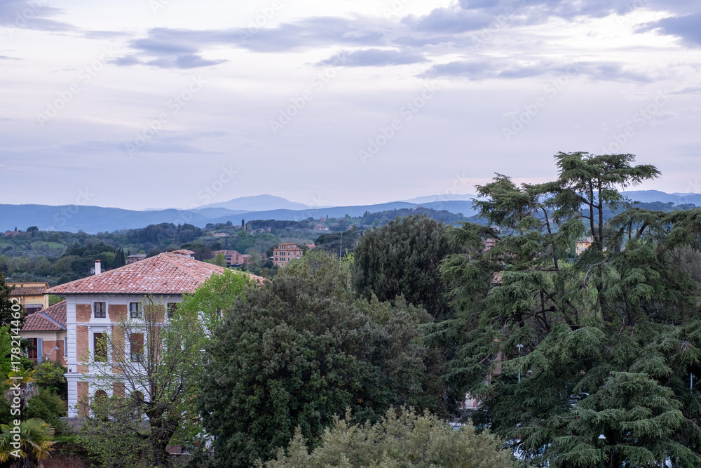 Obraz premium Scenic view of ancient stone buildings surrounded by lush greenery and distant hills, showcasing the historical charm and natural beauty of a captivating landscape