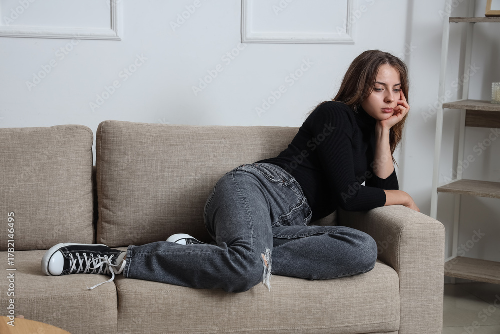 Obraz premium Sad young woman sitting on sofa at home