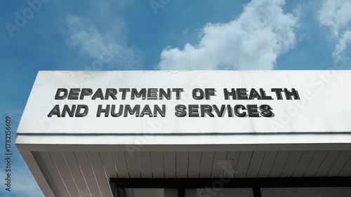 Department of Health and Human Services word sign displayed on a governmental building under a clear blue sky, symbolizing public health, social welfare, government aid, healthcare policy