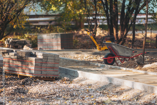 Construction site showing new pathway being built with bricks and wheelbarrow in a residential area during daytime