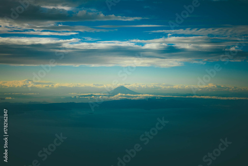 Distant view of Mount Fuji surrounded by layers of clouds seen from the sky