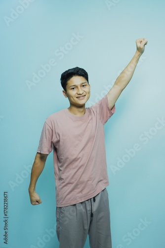Teen celebrates success with fist pump against a vibrant blue backdrop, radiating youthfulness and positive energy perfect for motivational concepts