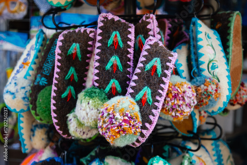 Fototapeta Naklejka Na Ścianę i Meble -  Creek colorful handmade wool slippers with traditional embroidery and pom-poms displayed at local market in Crete. Ethnic craftsmanship and folk art design. Original travel souvenirs from from Greece.