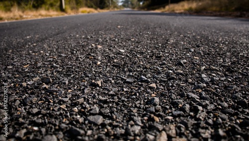 Fototapeta Naklejka Na Ścianę i Meble -  Close-up view of uneven asphalt featuring small stones and textures, highlighting erosion risk