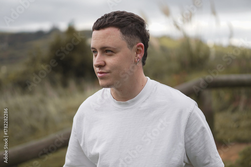 Young man in a white t-shirt looking at the horizon on a mountain path surrounded by nature