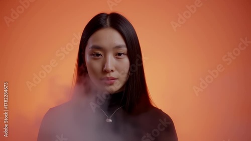 Asian Woman Exhaling Smoke in Studio with Orange Background.