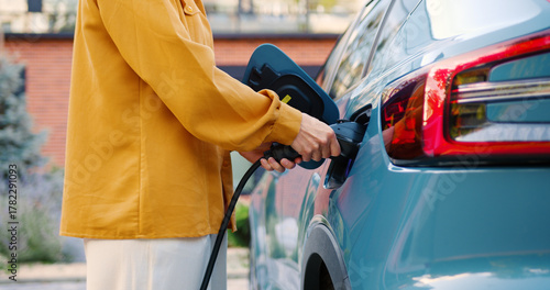 Close-up of female hands connecting an electric car charger to her vehicle outdoors