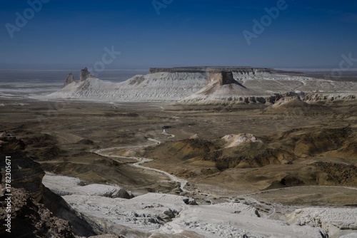 Kazakhstan, Bozzhira A vast desert landscape with white and brown rock formations, plateaus rising from the arid steppe beneath a clear, deep sky.